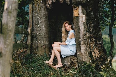 Jeune Jolie Fille Blonde Aux Pieds Nus En Robe Bleue Assise Dans Le Vieil Arbre Photo Premium