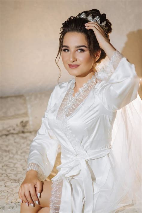 The Brunette Bride Dressed In A Satin Robe Sits On The Couch Beautiful Hair And Makeup Stock
