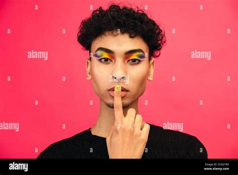 Gay Man Wearing Rainbow Colored Eye Shadow And Smiley Face Fingernail Putting His Finger In Lips