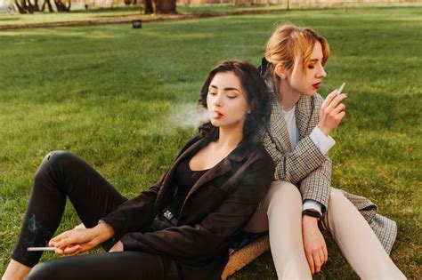 Premium Photo Two Pretty Women Friends Sitting On Grass Smoking Cigarette Couple Of Gay