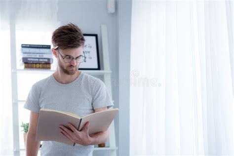 Handsome Guy In Eyeglasses Is Reading Book Preparing Exam And Thinking With Standing At The