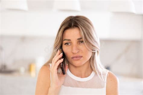 Irritated Blonde Talking On Phone While Sitting On Kitchen Table Stock Photo Image Of Phone