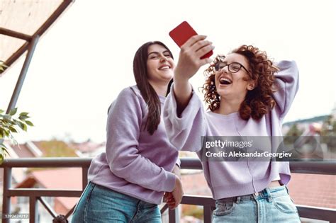 Two Smiling Female Friends Taking Selfie On Balcony High Res Stock