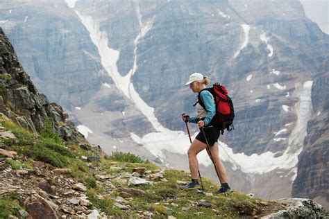 Female hiker with poles hiking up mountain path with mountain cliff ...