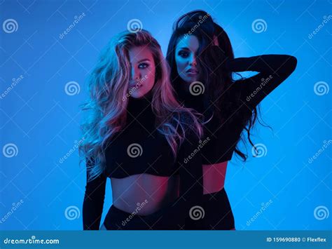 Blonde And Brunette Models In Black Clothes Looking At Camera And Posing In Studio Stock Photo
