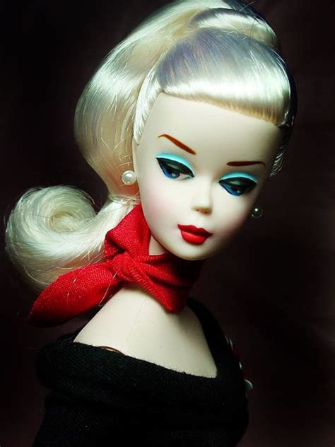 A Doll With Blonde Hair And Blue Eyes Wearing A Red Bow Around Her Neck