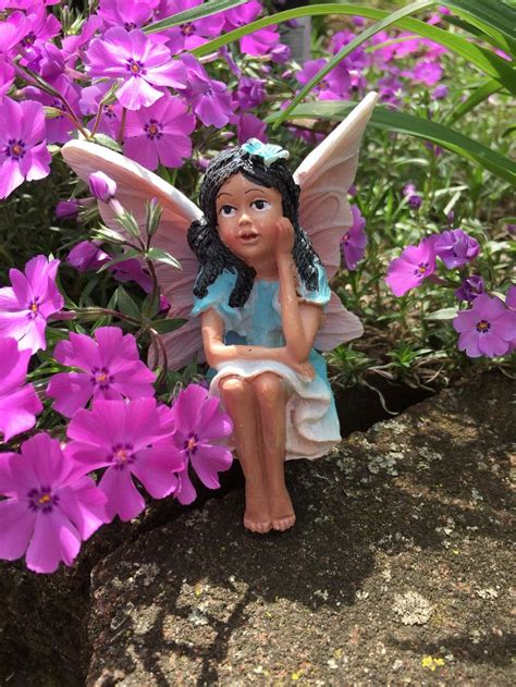 A Figurine Sitting On Top Of A Rock Next To Purple Flowers