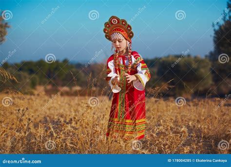 Small Cute Blonde Girl In Beautiful Traditional Russian Costume And Headdress Walking In Field