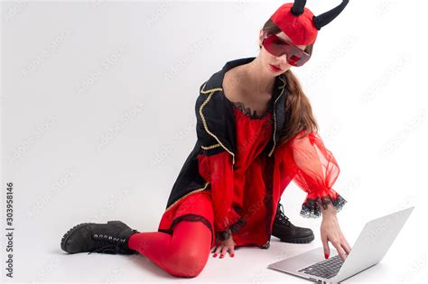 Sexy Brunette Woman In Red Tights Black Boots And Devil Horns Using Laptop Over White Studio