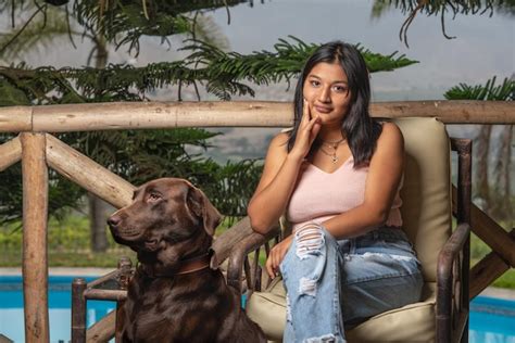 Mujer joven latina sentada en un sillón junto a un perro en una piscina Foto Premium