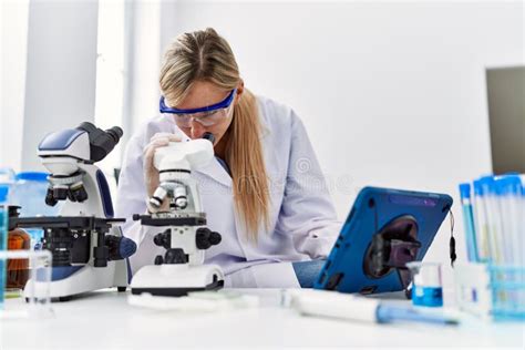 Junge Blonde Frau Mit Wissenschaftlicher Uniform Und Mikroskop Und Touchpad Im Labor Stockfoto