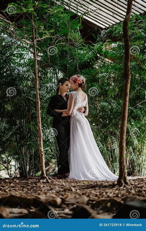 Vertical Of A Lesbian Pair Bride And A Female In Black Costume Holding Each Other Hand Stock