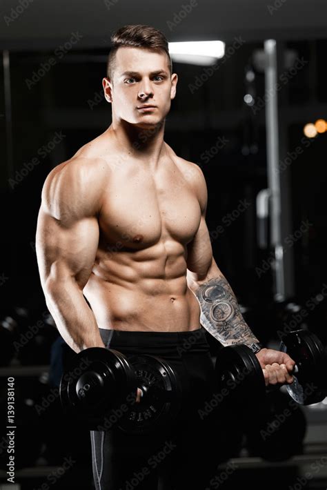 Male Bodybuilder Holding A Dumbbell In The Gym The Athlete With Naked Torso Stock Photo