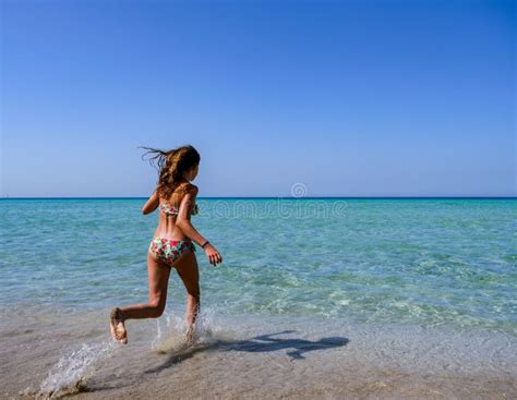 Beautiful Sporty Girl In A Colorful Bikini Running Into The Turquoise Water Of A Beautiful Beach