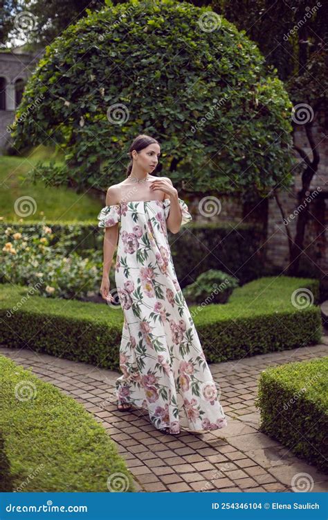Outdoor Portrait Of A Beautiful Luxury Brunette Woman In A Dress With Flowers Stands In A Park