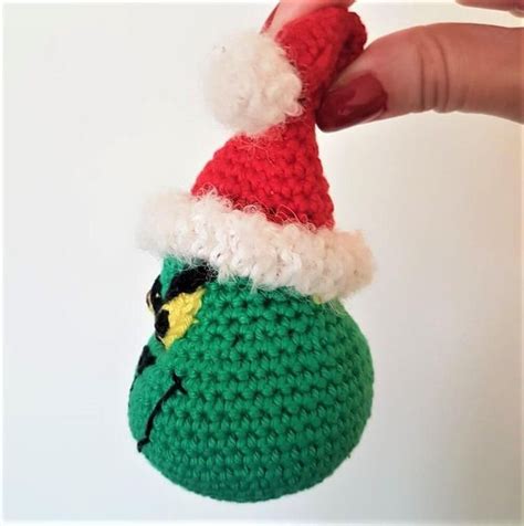 A Hand Holding A Crocheted Christmas Ornament With A Grin Face On It