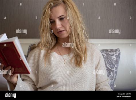 Belle femme blonde à la maison vêtements assis sur le lit et livre de lecture fermé papier