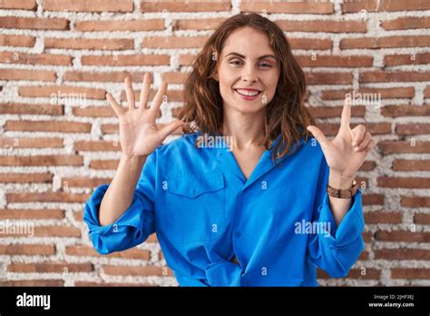 Beautiful Brunette Woman Standing Over Bricks Wall Showing And Pointing Up With Fingers Number