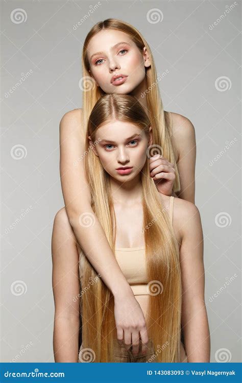 Two Blonde Beautiful Girls With Long Hair Looking At Camera In The Studio On A Bright Background