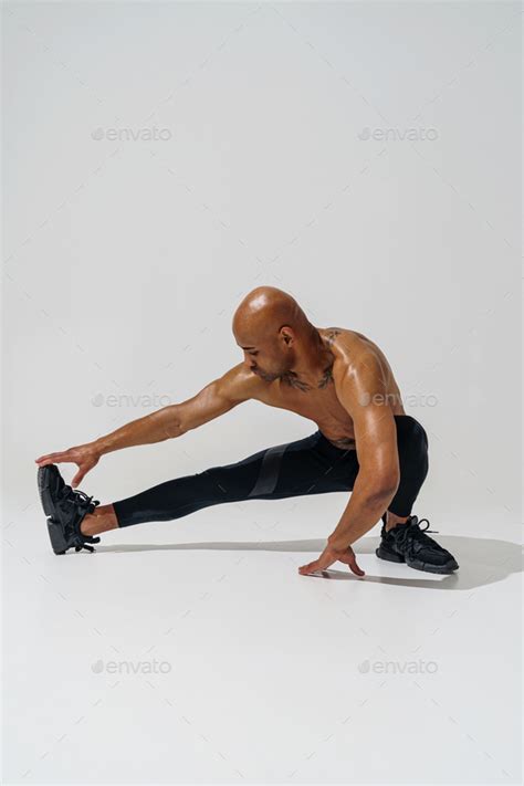 Athletic Man With Naked Torso Doing Leg Stretching Exercises Before Workout On Studio Background