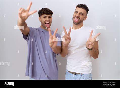 Homosexual Gay Couple Standing Over White Background Smiling With Tongue Out Showing Fingers Of