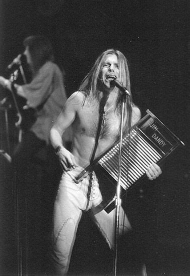 a man with long hair and no shirt on holding an accordion in front of him