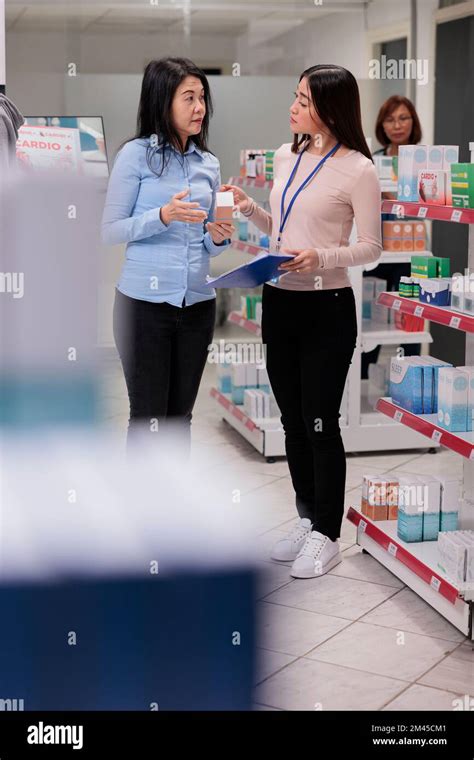 Pharmacy Assistant And Customer Examining Medicaments Looking At