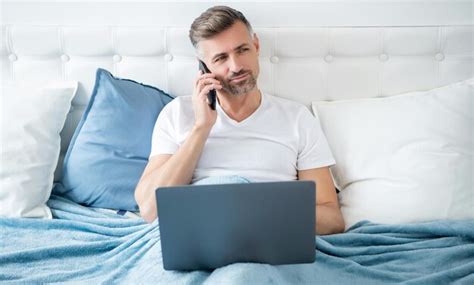 Premium Photo Mature Man Speak On Phone And Working On Laptop In Bed