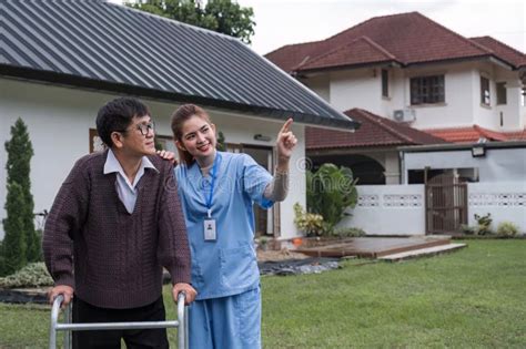 Asian Female Caregiver Helps Senior Man Walk A Senior Using A Walker Is