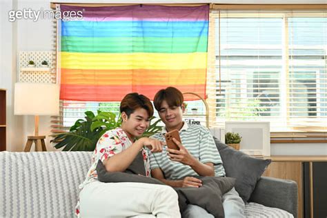 Loving young gay couple using mobile phone on sofa enjoy spending weekend together 이미지