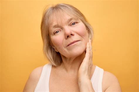 A Woman With Blonde Hair Showcases A Serene Expression While Lightly Touching Her Cheek The