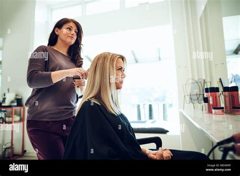 Coiffure Styling Les Cheveux D Une Jeune Femme Blonde Assise Sur Une Chaise Tout En Travaillant