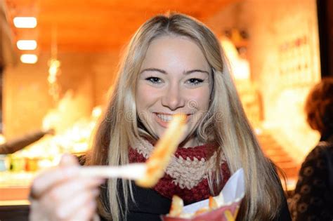 Cheerful Blonde Woman Visits A Fun Fair Or Christmas Market At Night And Eats A Snack Stock