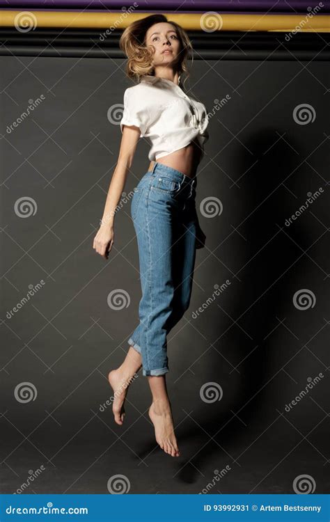 Portrait D Une Blonde Aux Pieds Nus De Fille Dans La Chemise Et Des Jeans Blancs Dans Le Saut