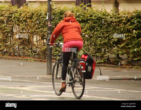 A Back Shot Of A Blonde Girl Riding A Bicycle In The Street With Trees In Frankfurt City