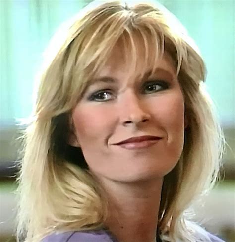 A Woman With Blonde Hair And Blue Eyes Looks Off To The Side While Wearing A Purple Shirt