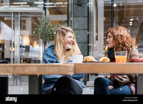 Zwei junge schöne Blonde und Rothaarige Frauen frühstücken im freien Chat und lächelnd Glück