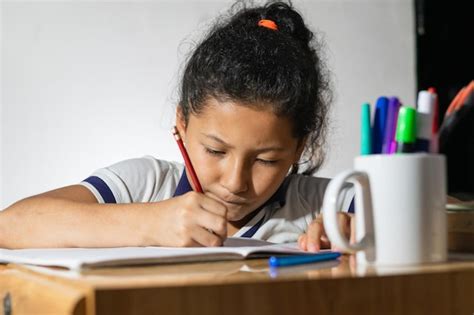 Niña estudiante latina haciendo su tarea muy concentrada y rápida en un escritorio de madera