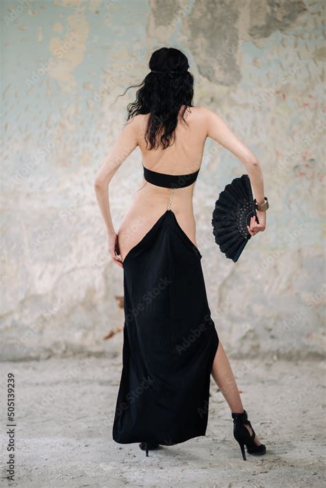 Sexy Brunette Girl Stands With Her Back With A Fan In A Black Dress Of Her Own Making Stock
