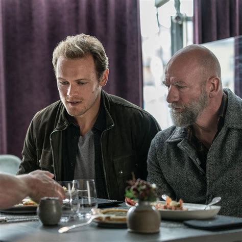 Two Men Sitting At A Table With Food In Front Of Them And One Man