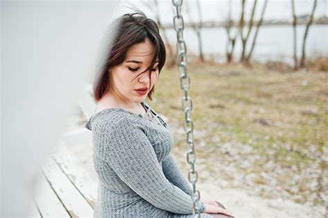 Portrait Of Brunette Girl In Gray Dress Sitting At White Wooden Construction Stock