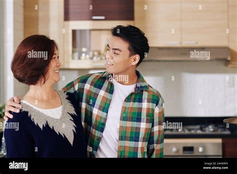 Happy Hugging Mature Mother And Her Adult Son Standing In Kitchen Hugging And Looking At Each