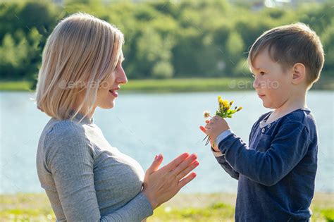 Cute Baby Son Gives A Gift Flowers To His Beautiful Blonde Mother In The Park Stock Photo By