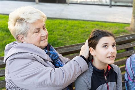 Grand mère blonde faisant les cheveux de petite fille assise sur un banc de parc Photo Premium