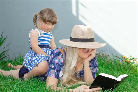 La Blonde De Maman Dans Un Chapeau Et Sa Fille Se Trouvent Sur L Herbe Et Lisent Un Livre