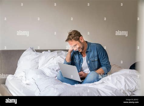 Smiling Mature Man Sitting On His Bed Using Laptop Stock Photo Alamy