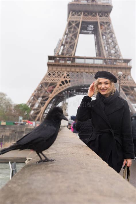Lady In Total Black Outfit Smile While Looking At Crow On Background Of Eiffel Tower Blonde
