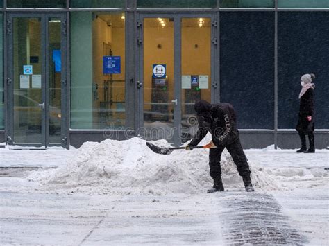 A Utility Worker Shovels Snow With A Shovel On A City Street During A