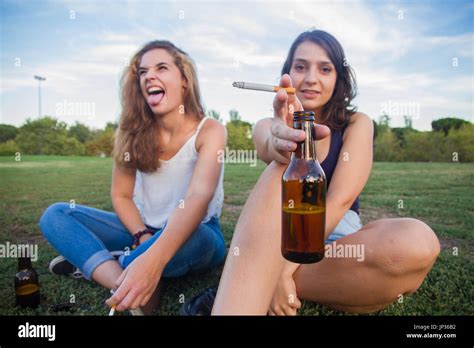 Two girls, friends, smoking cigarettes and drinking beer bottles in ...