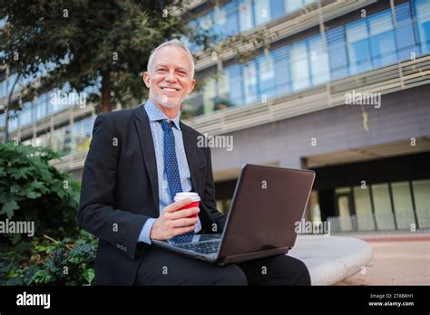 Mature Handsome Businessman In Suit Using A Laptop Computer Sitting Outside The Office Relaxing